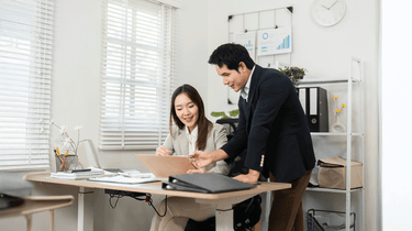 Two active professionals discussing work at a desk in an office setting. Camel Nuts Singapore