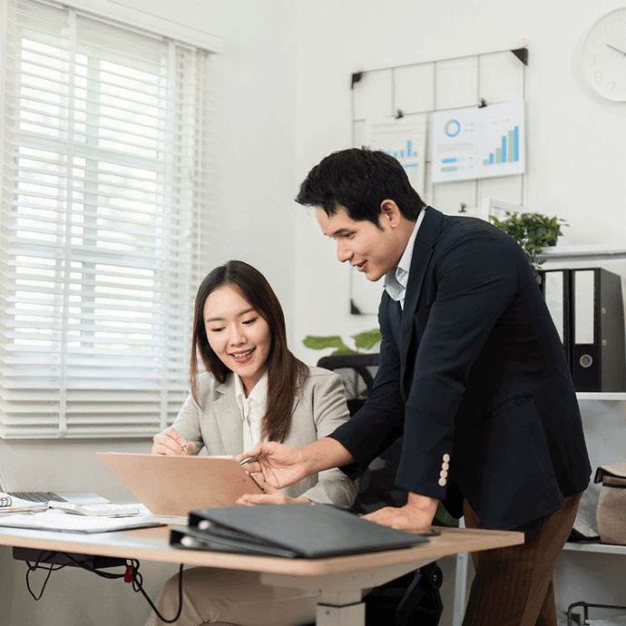 Two active professionals in a modern office setting, discussing work on a laptop.