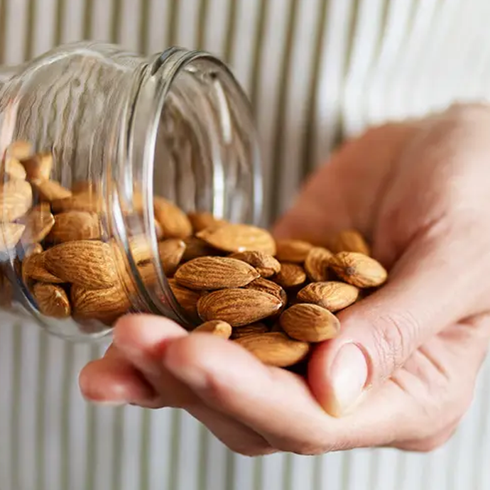 Hand holding Camel Nuts almonds with a glass jar tipped over, showing more almonds.