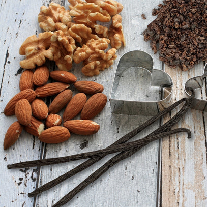 Almonds and walnuts, vanilla beans, and metal cookie cutters on a wooden surface. Camel Nuts Singapore