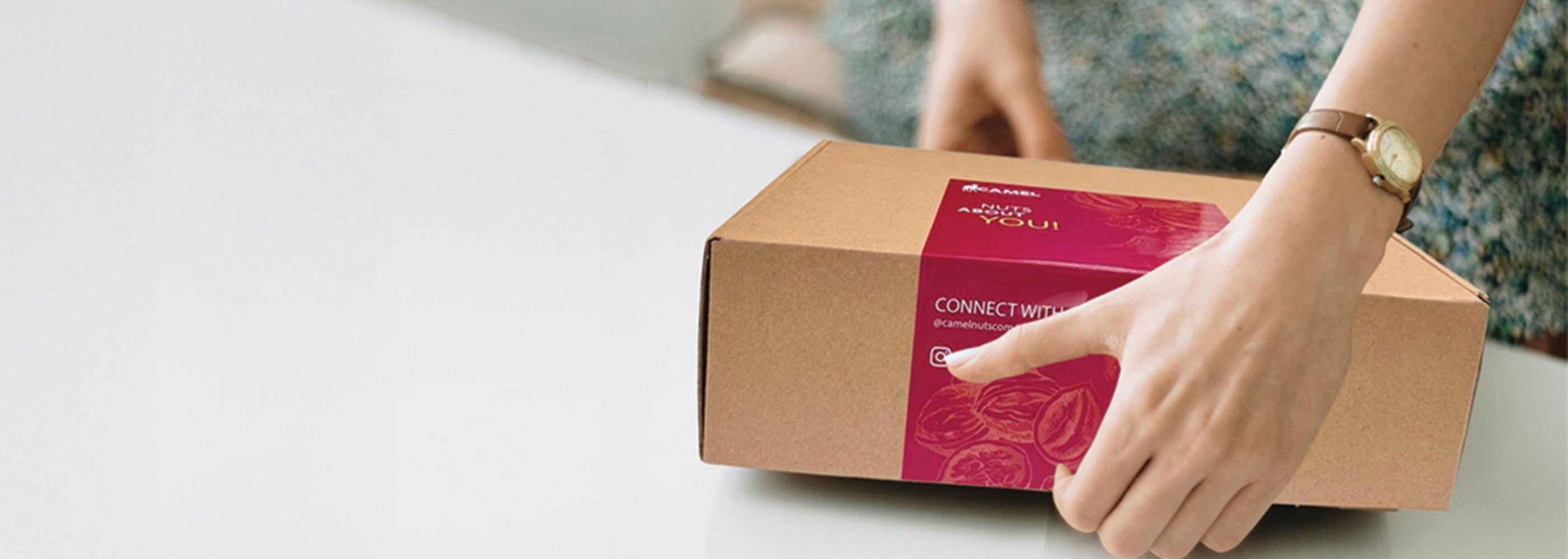 Woman opening a cardboard box with a Camel Nuts red label. Ideal for corporate events and gifts