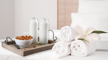 White towels on a white surface with a wooden tray holding a bowl of nuts and two glass bottles. Camel Nuts Singapore