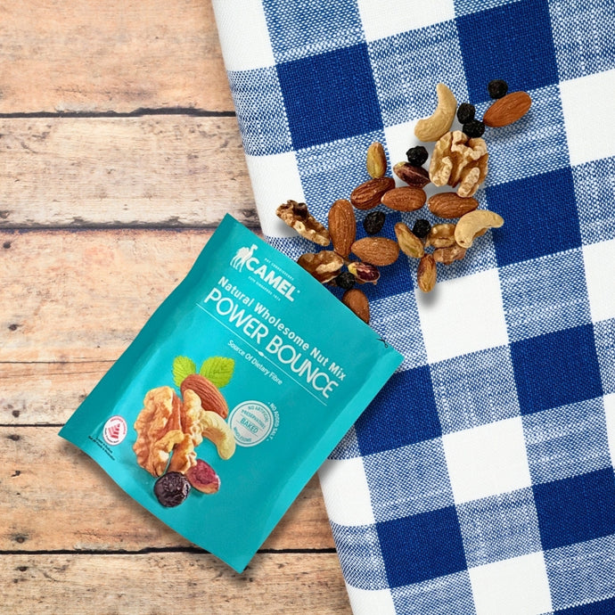 Camel Nuts Power Bounce natural whole grain nut mix packet on a checkered cloth with nuts spilling out.