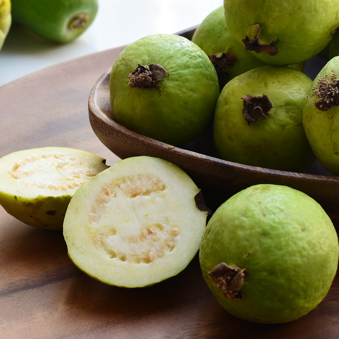 Green guava fruits on a wooden plate with one halved guava showing its interior.