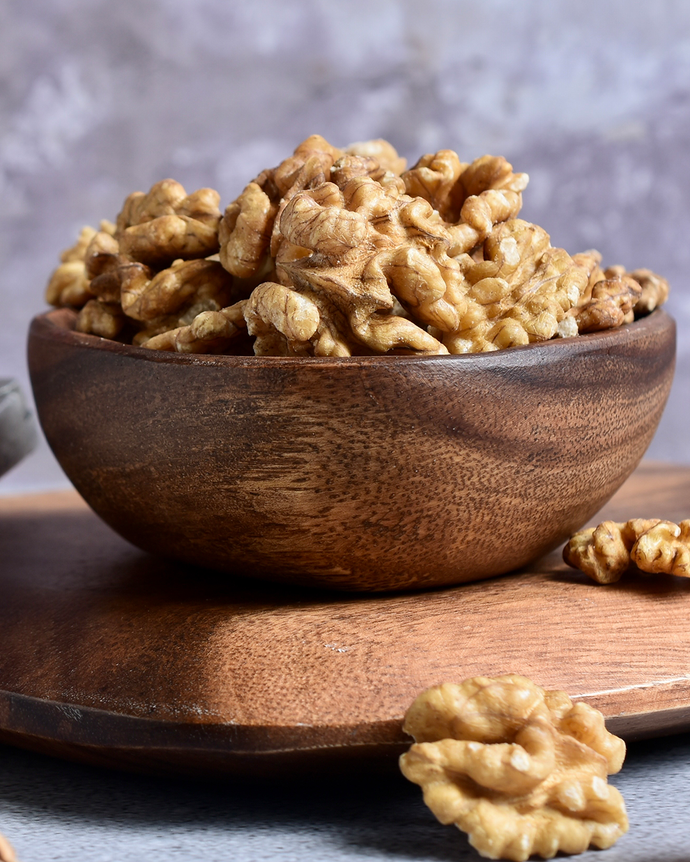 Wooden bowl filled with walnuts on a wooden surface with a blurred background. Camel Nuts Singapore