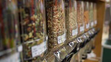 Row of dispenser jars with various types of nuts and seeds on a shelf. At Camel Nuts we have the best variety of nuts for your business. Wholesale orders here.