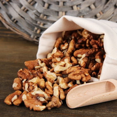 Walnuts spilling out of a white bag with a wooden scoop on a wooden surface. Camel Nuts Singapore