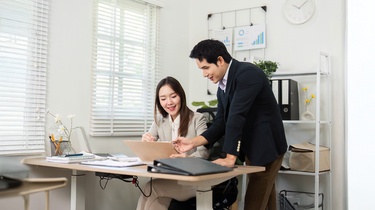 Two active professionals discussing work at a desk in an office setting. Camel Nuts Singapore