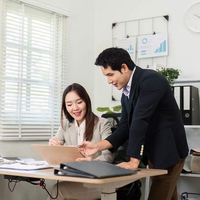 Two active professionals in a modern office setting, discussing work on a laptop.