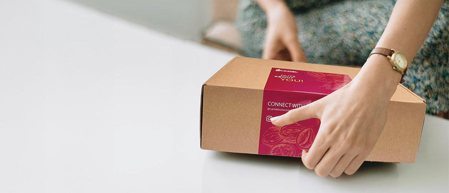 Woman opening a cardboard box with a Camel Nuts red label. Ideal for corporate events and gifts