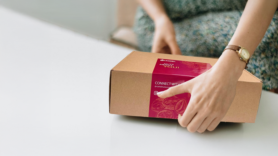Woman opening a cardboard box with a Camel Nuts red label. Ideal for corporate events and gifts