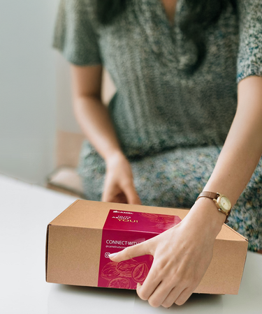 Woman holding a Camel Nuts cardboard box with a red label. Make an impression in corporate events and gifts!