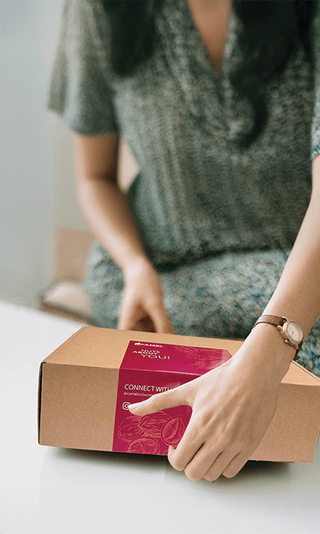 Woman holding a Camel Nuts cardboard box with a red label. Make an impression in corporate events and gifts!