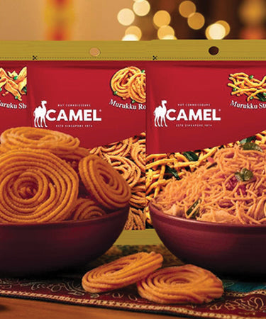 Camel Nuts muruku snack packages on a decorative table with festive lights in the background to celebrate Deepavali