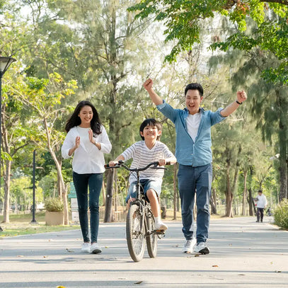Family of three with a child on a bicycle in a park. Camel Nuts Singapore
