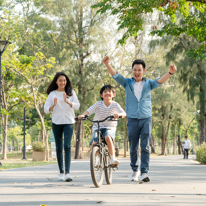Family of three with a child on a bicycle in a park. Camel Nuts Singapore