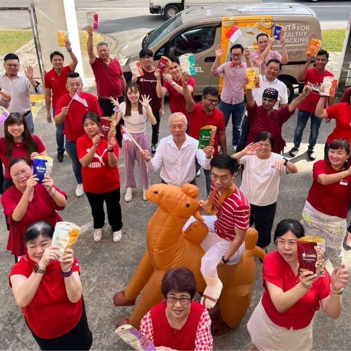 Group of people in red shirts holding CAmel Nuts products with a person in a camel costume in the center.