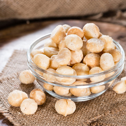 Singapore's Camel Nuts macadamias in glass bowl – Bowl of salted macadamias on a rustic wooden table.