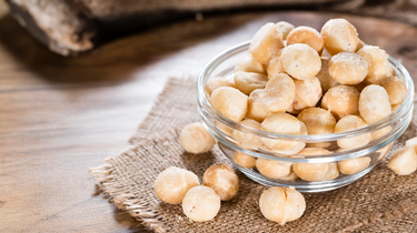 Camel Nuts Singapore macadamias in glass bowl – Bowl of salted macadamias on a rustic wooden table.