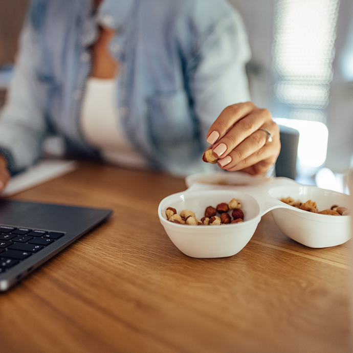 Person eating premium hazelnuts from small bowls on a desk with a laptop.