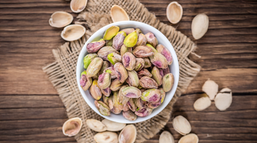 Camel Nuts Singapore shelled pistachios in bowl – White bowl of shelled pistachios on rustic burlap with empty shells around.
