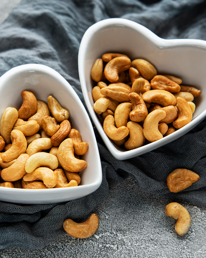 Camel Nuts Singapore cashews in heart bowls – Two heart-shaped bowls filled with cashews on textured fabric.