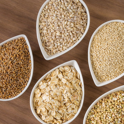 Five white bowls filled with different types of seeds and grains on a wooden surface. Camel Nuts Singapore