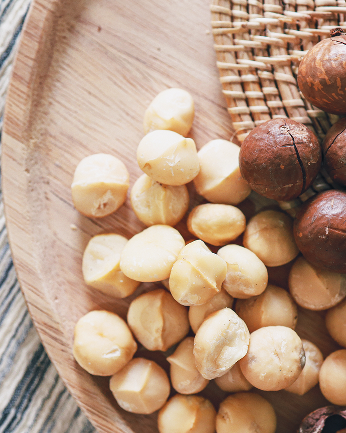 Camel Nuts Singapore macadamias on wooden plate – Shelled and whole macadamias on a wooden plate with woven mat.