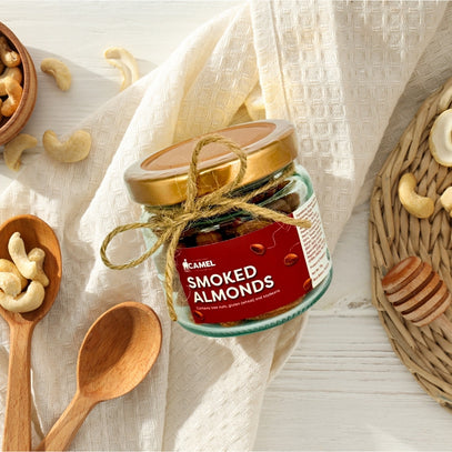 Jar of Camel Nuts Smoked Almonds with wooden spoons and cashews on a light fabric background. Great idea for a wedding or party favors. Camel Nuts Singapore