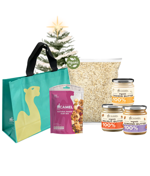 Camel Oaty Breakie Festive Set featuring a teal reusable bag with camel logo, a pack of natural baked Ruby Mix, a large pack of organic oats, and three jars of 100% organic nut butter (almond, walnut, and cashew), displayed with a small Christmas tree in the background.