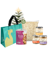 Camel Oaty Breakie Festive Set featuring a teal reusable bag with camel logo, a pack of natural baked Ruby Mix, a large pack of organic oats, and three jars of 100% organic nut butter (almond, walnut, and cashew), displayed with a small Christmas tree in the background.