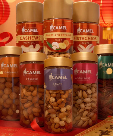 Caramel cashew nuts in glass jars on a red tablecloth with red lanterns and gift boxes, blurred lights in the background.